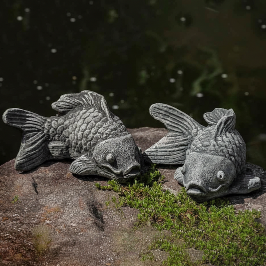 Two stone fish sculptures on a rock with water in the background