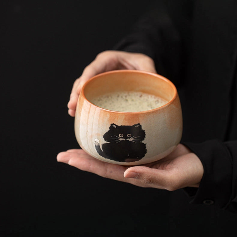 Person holding a ceramic bowl with a cat design on a black background