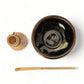 Black ceramic bowl with wooden whisk and spoon on a white background