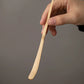 Bamboo matcha spoon being held against a gray background.