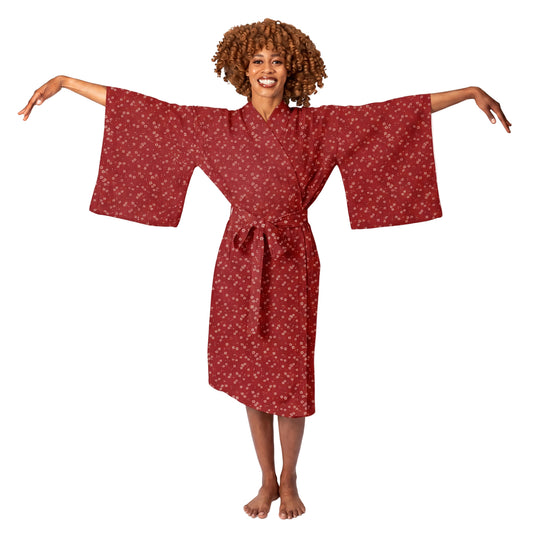 A woman modeling a red kimono-style robe with a small white floral pattern, standing against a plain white studio background with her arms outstretched.