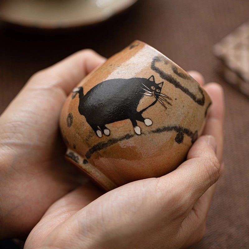 Tea cup with a black cat painted on it being held in hands.