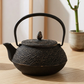 Black cast iron teapot and cup on a wooden table with a plant in the background