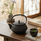 Tea set with black teapot, cup, and whisk on a wooden table with a blurred background