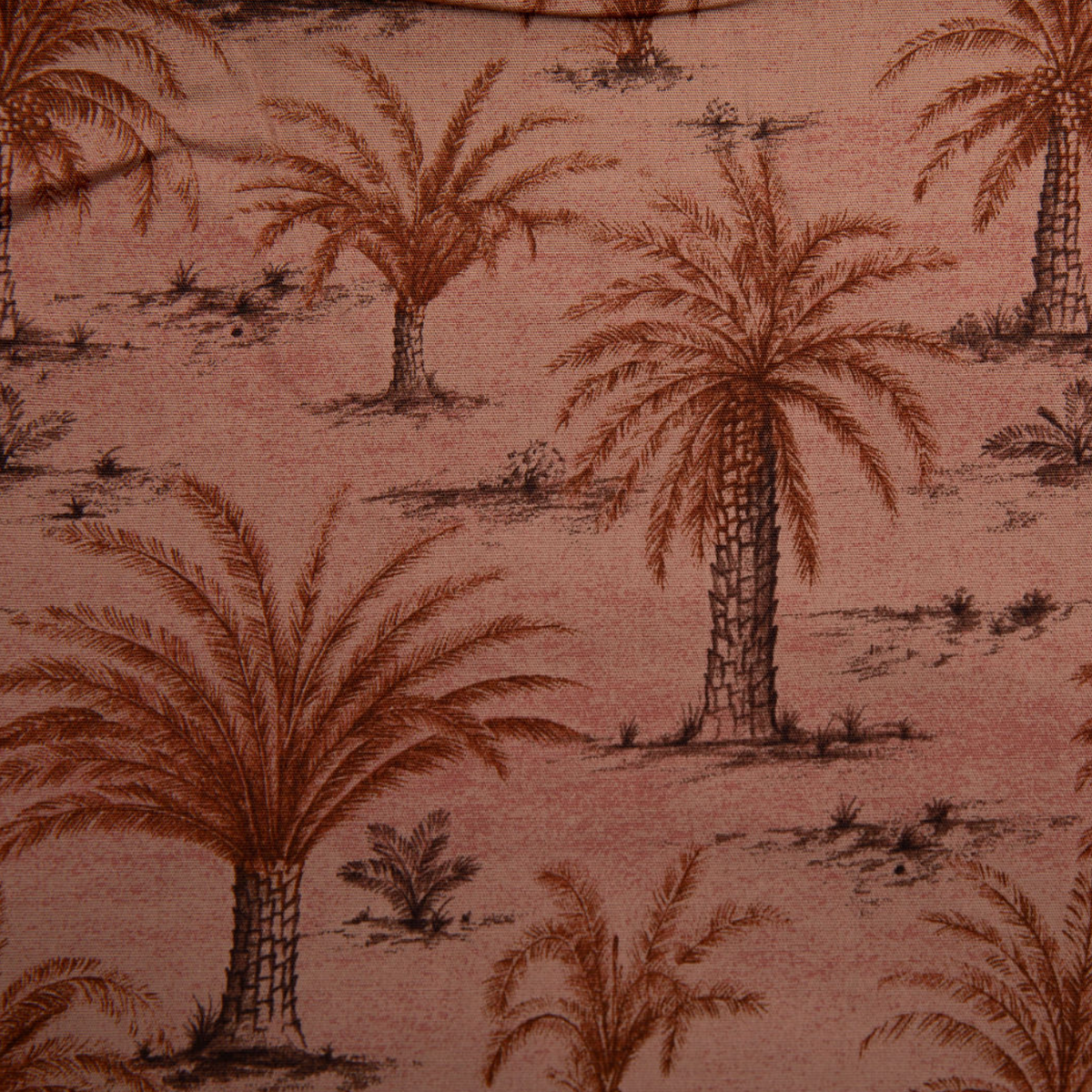 A close-up of a fabric pattern featuring brown palm trees and small desert plants on a dusty pink background.