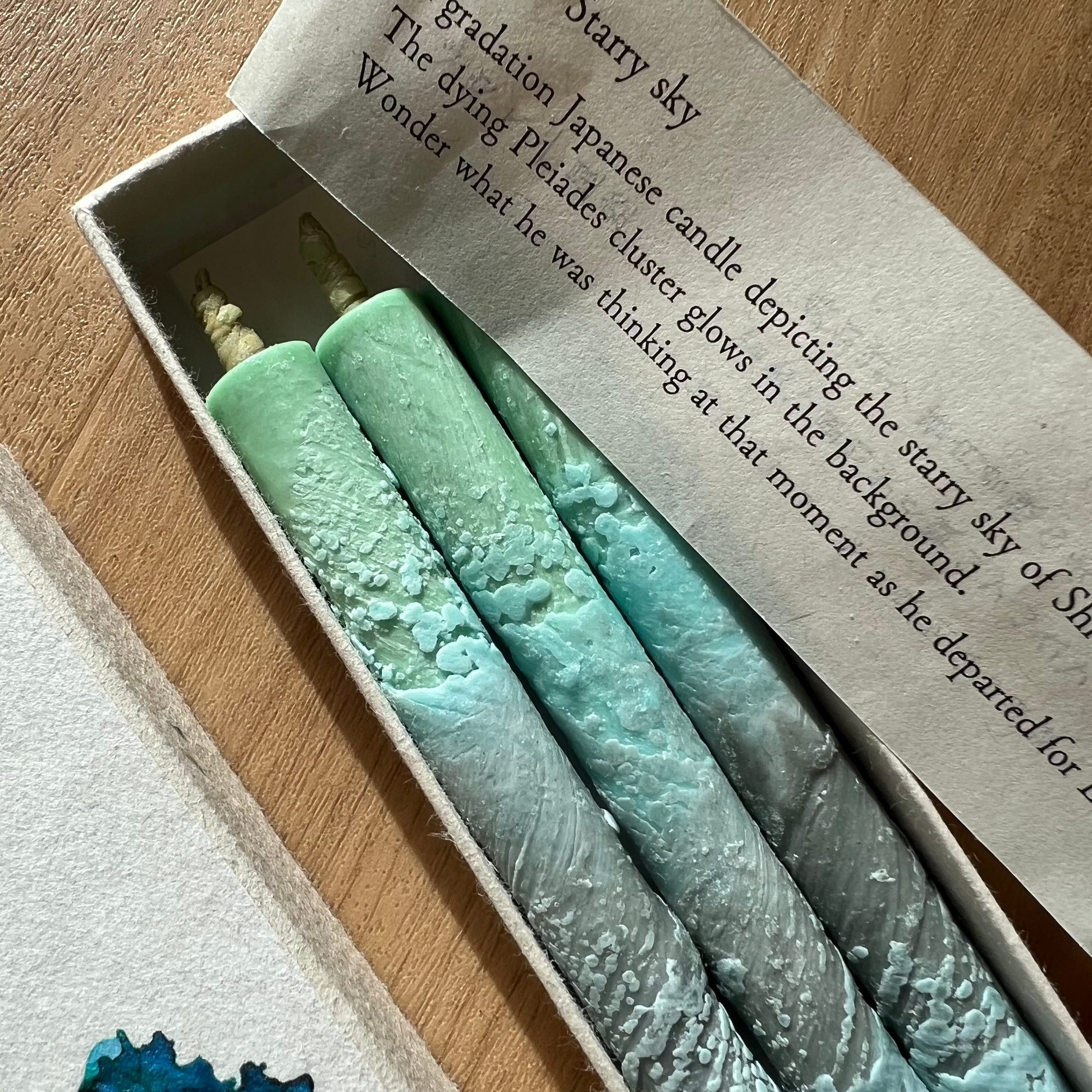 Three gradient candles in a box with a label on a wooden surface