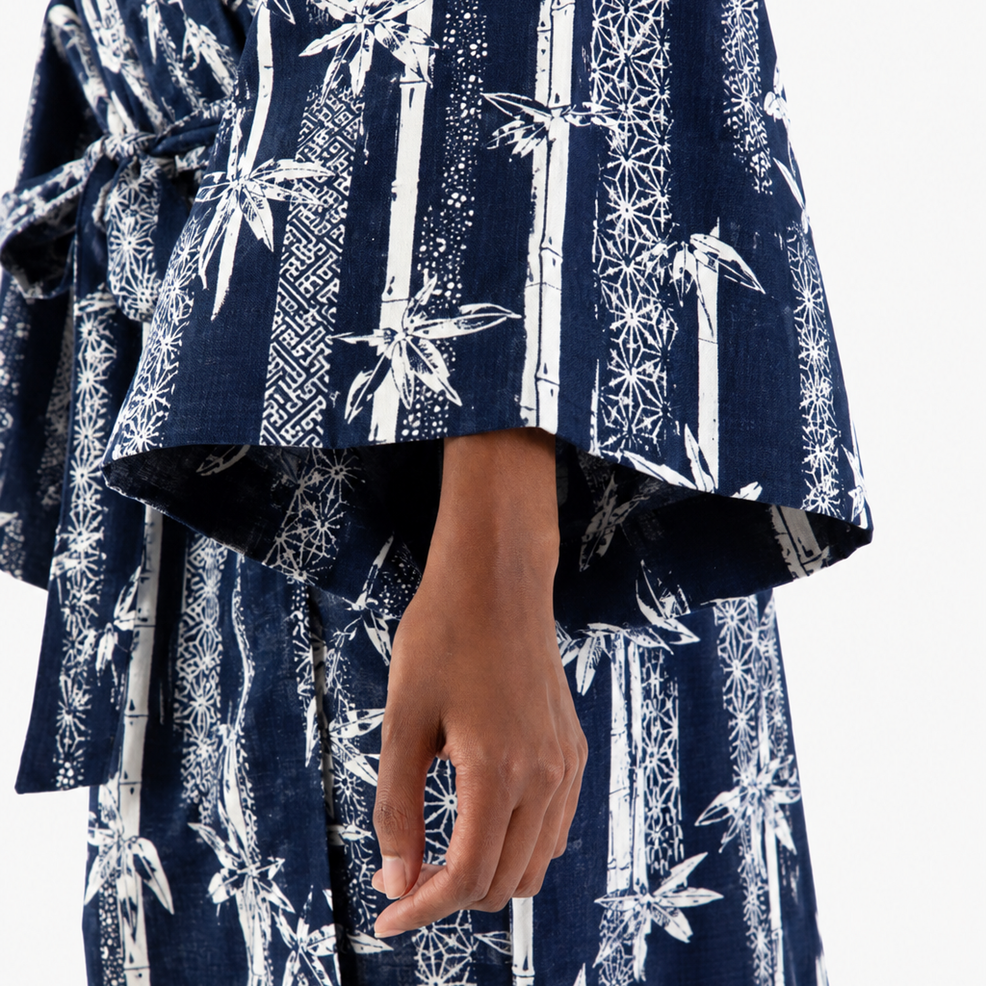 A close-up of a person wearing a navy blue and white patterned robe or kimono-style garment, with wide flared sleeves and a visible hand against a plain light background.
