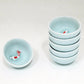Set of small light blue tea cups with fish figurines on a white background