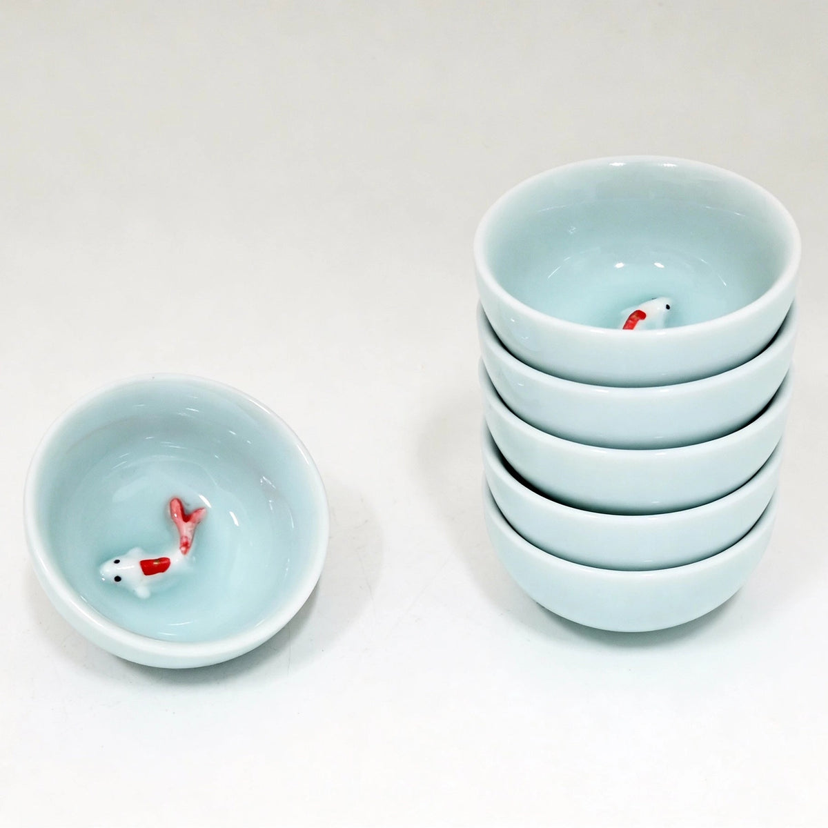 Set of small light blue tea cups with fish figurines on a white background