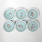 Six small white ceramic cups arranged in two rows of three on a plain white background, each filled with pale aqua water and containing a small white fish with red accents.