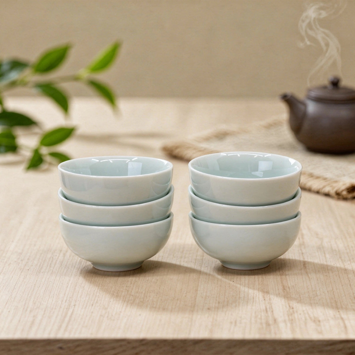Set of white ceramic bowls on a wooden surface with a teapot and plant in the background.