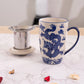 White mug with blue dragon design on a marble surface with tea accessories.