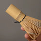 Bamboo whisk held by a hand against a gray background