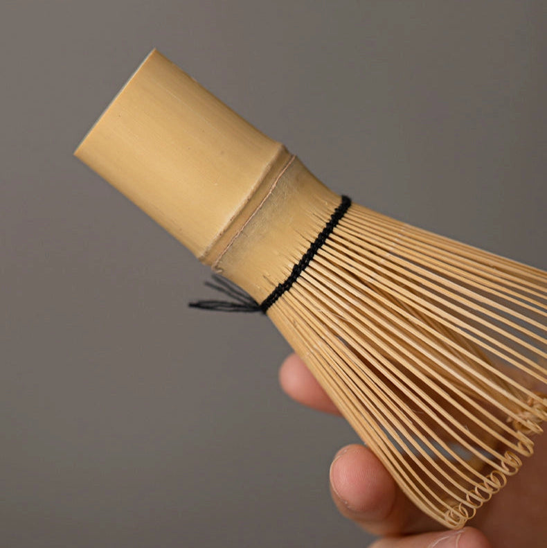 Bamboo whisk held by a hand against a gray background