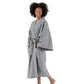 A woman wearing a long-sleeved patterned bathrobe with a matching waist tie, standing barefoot against a plain white studio background.