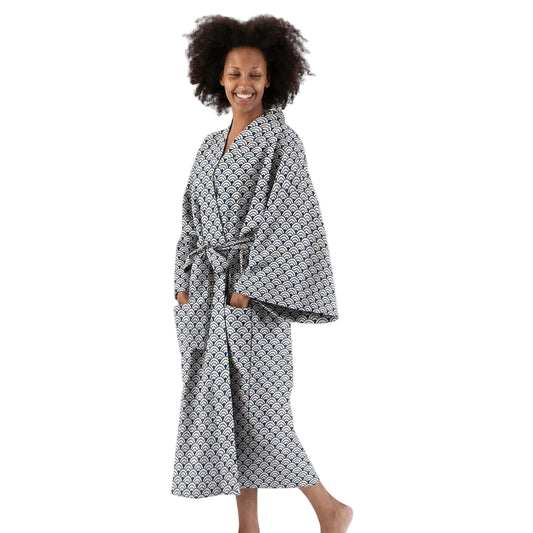 A woman wearing a long-sleeved patterned bathrobe with a matching waist tie, standing barefoot against a plain white studio background.