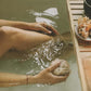 Person relaxing in a hot tub with a coconut, surrounded by wooden elements.